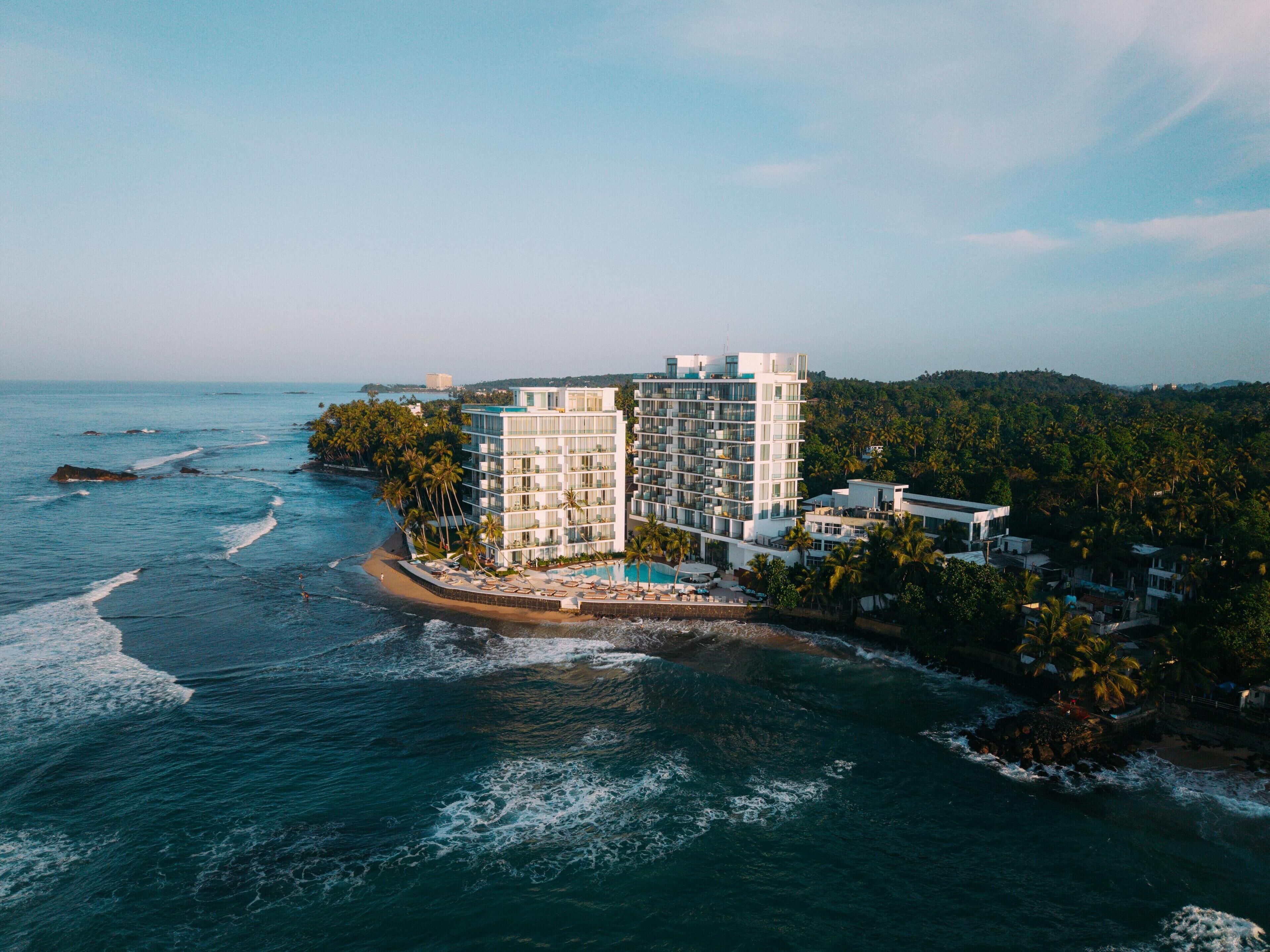 A coastal hotel with multiple floors, a pool, and a view of the ocean.