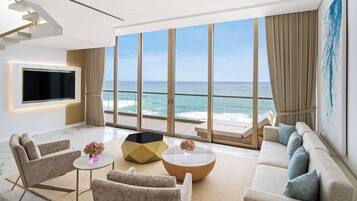 A modern living room with a large window overlooking the ocean, a flat-screen TV mounted on the wall, and a comfortable seating area with sofas and a coffee table.