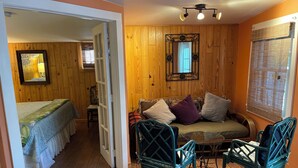 A cozy room with a wooden floor, a bed with floral bedding, a green sofa with cushions, and two green chairs around a small table. - Pool, laundry, and grilling area (Key West)