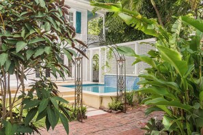 Un'area piscina con recinzione bianca, una piccola cascata e vegetazione lussureggiante.