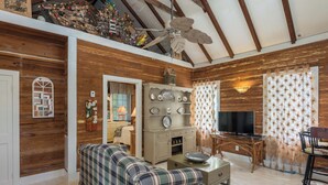 Un accogliente soggiorno con pareti in legno, una ventola a soffitto, un divano a quadri, una TV e un'area pranzo con tavolo e sedie.