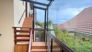 A wooden staircase with glass railings leading to a balcony overlooking a garden and neighboring buildings. - THE WRITERS HOUSE (Campos do Jordão)
