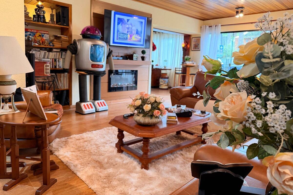 Ein gemütliches Wohnzimmer mit Kamin, Fernseher, Bücherregal und Couchtisch mit Blumen.