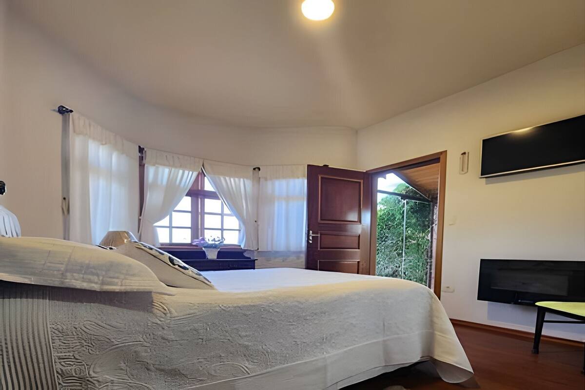 Ein Schlafzimmer mit einem Bett, einem Fernseher, einem Fenster mit Vorhängen und einer zur Außenseite führenden Tür.