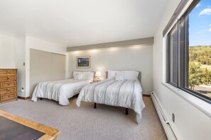 Een slaapkamer met twee bedden, een dressoir, een schilderij en uitzicht op bomen.
