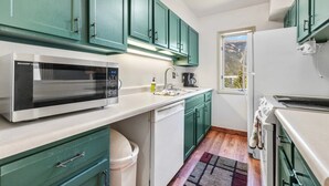 Cocina compacta con armarios color turquesa, microondas, cafetera y ventana con vistas.