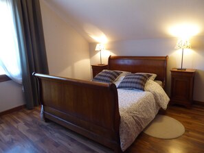 A bedroom with a wooden bed, two bedside lamps, a round rug, and a window with curtains.