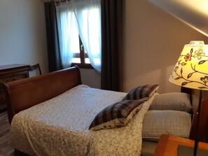A bedroom with a bed, a bedside table with a lamp, a window with curtains, and a chair.