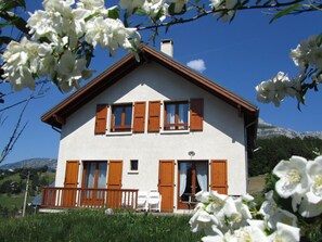 Een tweelaags huis met een balkon, houten luiken en een berg op de achtergrond.