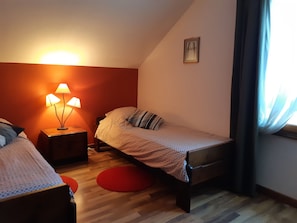 Een slaapkamer met twee bedden, een nachtkastje met lampen, een klein schilderij aan de muur en een raam met gordijnen.