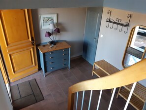 Een kamer met een houten deur, een blauwe ladekast, een lijst met een foto aan de muur en een klein houten krukje.