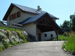 Een huis met twee verdiepingen, een schuin dak, een overdekte veranda en een stenen muur.