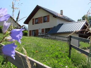 Ein zweigeschossiges Haus mit geneigtem Dach und Holzzaun vor der Fassade.