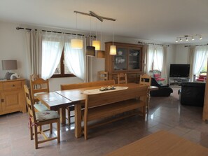 Een eetgedeelte met een houten tafel en stoelen, een kast met glazen deuren, en een televisie in de woonkamer.