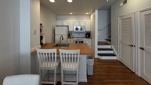 Una cocina compacta con armarios blancos, encimera de madera y un lavabo. Hay dos sillas blancas en la encimera.