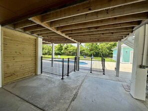 A covered outdoor area with a concrete floor, a wooden door, and a metal fence.