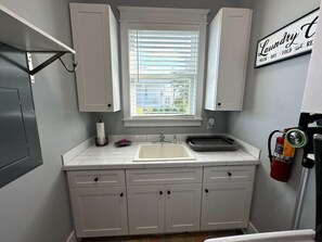 A small kitchen with a sink, cabinets, a window with blinds, a fire extinguisher, and a sign that says 'Laundry.'