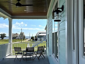 A covered porch with a table and chairs, overlooking a residential area with houses and a clear sky. - Walk to Beach | Private Pool | Sleeps 8 (Long Beach)