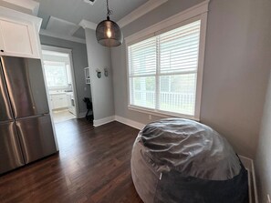 A kitchen with a stainless steel refrigerator, a dark wooden floor, a hanging light fixture, and a window with blinds.