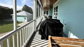 Une véranda abritée avec un barbecue, un banc en bois et une vue sur une maison et une pelouse.