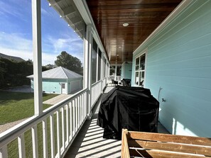 A covered porch with a grill, a wooden bench, and a view of a house and lawn. - Walk to Beach | Private Pool | Sleeps 8 (Long Beach)