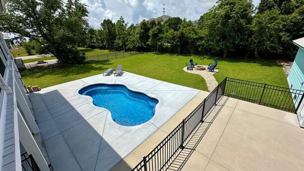 Un jardin à l’arrière d’une maison d’habitation, avec une piscine, une zone délimitée par une clôture et la maison elle-même.
