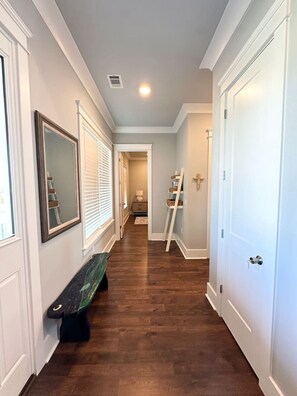 A hallway with wooden flooring, white walls, and a door on the right. - Walk to Beach | Private Pool | Sleeps 8 (Long Beach)