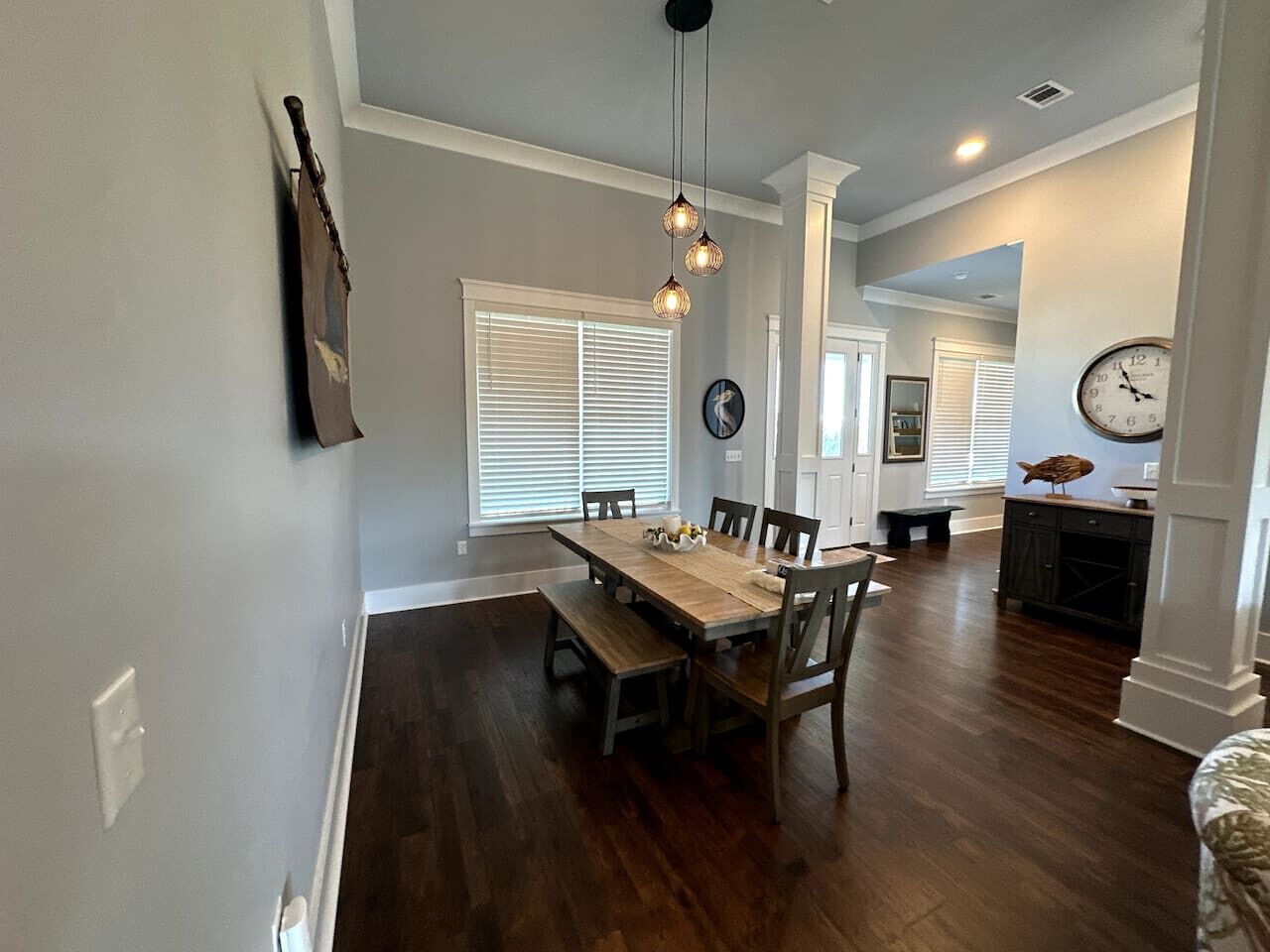 A dining area with a wooden table and chairs, a hanging light fixture, and a clock on the wall.