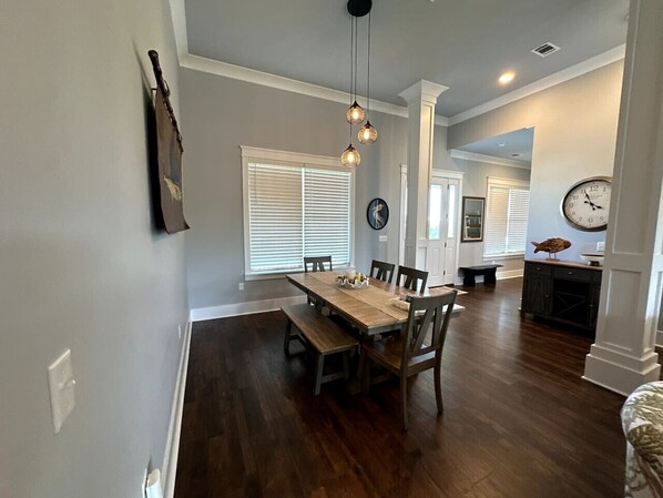 A dining area with a wooden table and chairs, a hanging light fixture, and a clock on the wall.