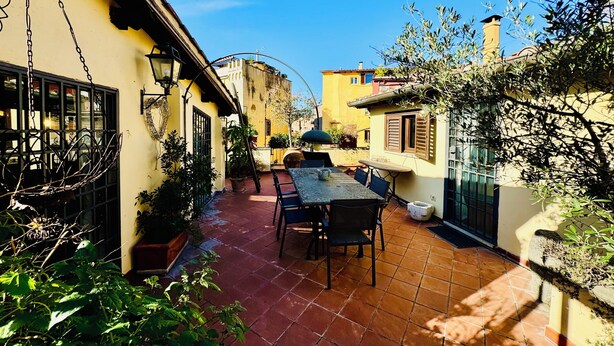 A courtyard with a table and chairs, surrounded by buildings with yellow walls and a tiled floor. - Roody Luxury house in Trastevere (Rome)