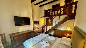 A bedroom with a bed, a TV mounted on the wall, a wooden staircase, and a bedside table with a lamp. - Roody Luxury house in Trastevere (Rome)