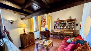 A cozy living room with a red sofa, a wooden coffee table, a bookshelf, and a dining area with a table and chairs. - Roody Luxury house in Trastevere (Rome)