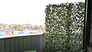 Un balcon avec une table et des chaises en métal vert, une clôture en métal et une vue sur des bâtiments en arrière-plan.