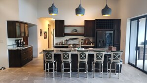 A modern kitchen with dark cabinetry, a central island with bar stools, and pendant lighting. - Spacious 5-bedroom ocean view villa in Dominicalito  (Puntarenas Province)