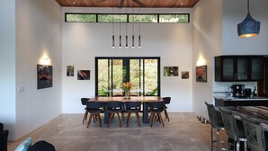 A dining area with a large table, chairs, and a view through a window. - Spacious 5-bedroom ocean view villa in Dominicalito  (Puntarenas Province)
