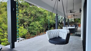 A modern outdoor seating area with a hanging chair, a dining table, and a view of lush greenery. - Spacious 5-bedroom ocean view villa in Dominicalito  (Puntarenas Province)