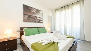 A neatly made bed with a green throw blanket and a white towel arranged on it.