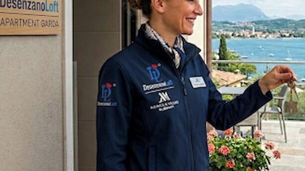 A person standing at a hotel entrance with a sign reading 'Desenzano Loft APARTMENT GARDEN'.