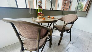 Een balkon met rieten stoelen en een ronde tafel, met een decoratief Sint-Nicolaasbeeldje en een kleine plant.