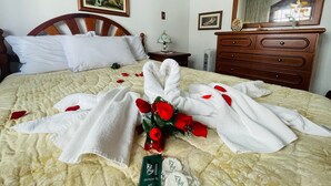 Een hotelkamer met een bed, een houten dressoir, een nachtkastje, een lijst met een afbeelding aan de muur, en een bos rode rozen op het bed.