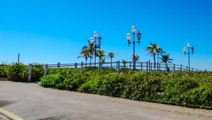 A paved walkway with a metal railing, palm trees, and street lamps. - Pousada Nereidas (Guaratuba)