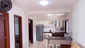 A compact kitchen with a refrigerator, microwave, and sink. There is a wooden door leading to another room, and a small seating area with a sofa and stools. - Pousada Nereidas (Guaratuba)