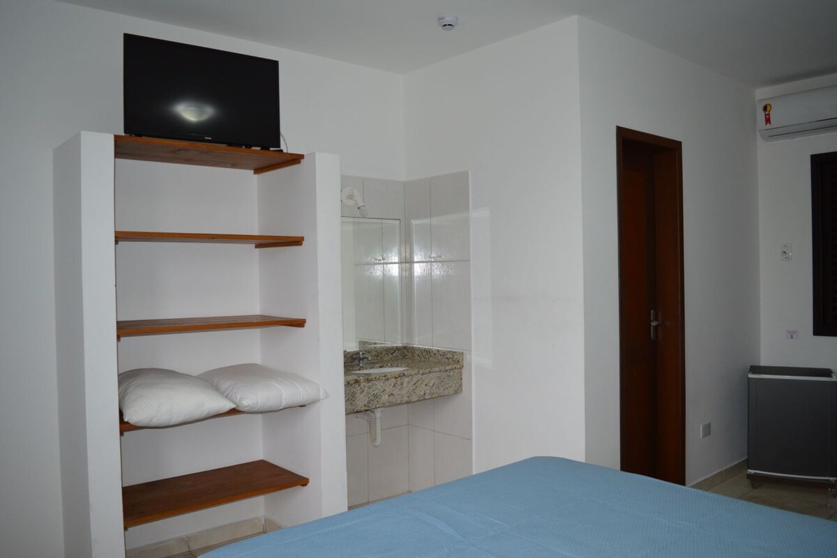 A bedroom with a bed, a wardrobe with shelves, a mirror, a sink, and a door.