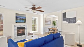 A spacious living room with a fireplace, a blue sofa, a dining area, and a ceiling fan.