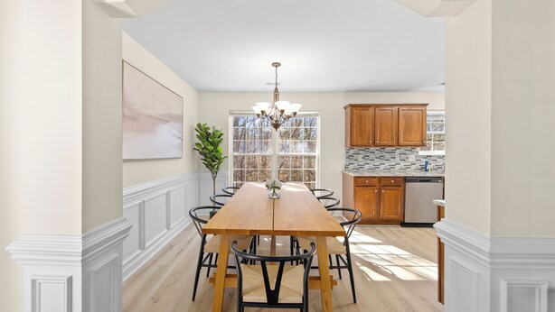 A dining room with a wooden table and chairs, a chandelier, and a view of the kitchen.