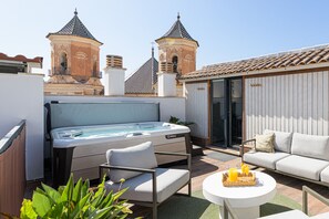 A rooftop terrace with a hot tub, a sofa, a coffee table, and a view of a historic building with towers.