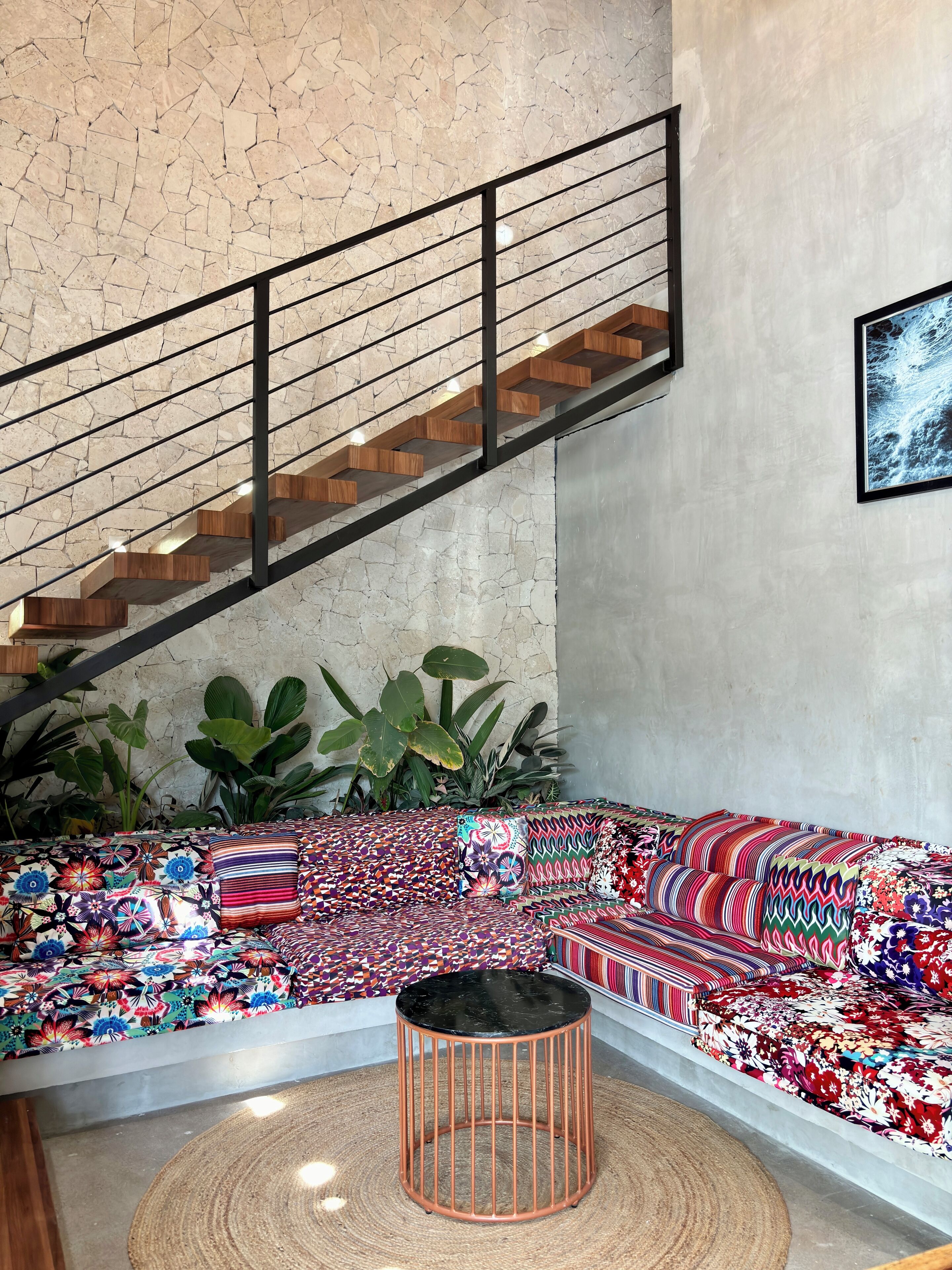 A modern living space with a wooden staircase, a colorful patterned sofa, and large green plants.