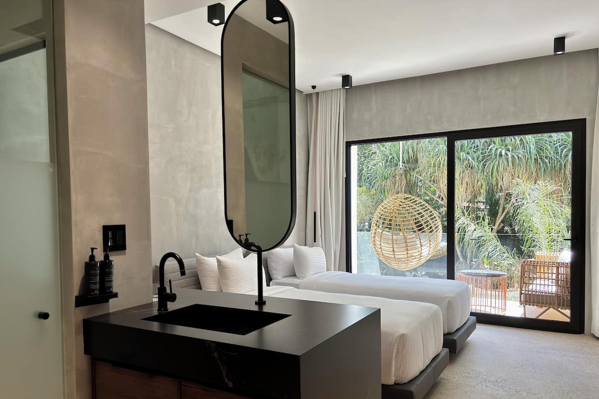 Une chambre moderne avec un grand lit, une coiffeuse noire avec un miroir, et une vue sur un jardin luxuriant grâce à une porte-fenêtre coulissante.