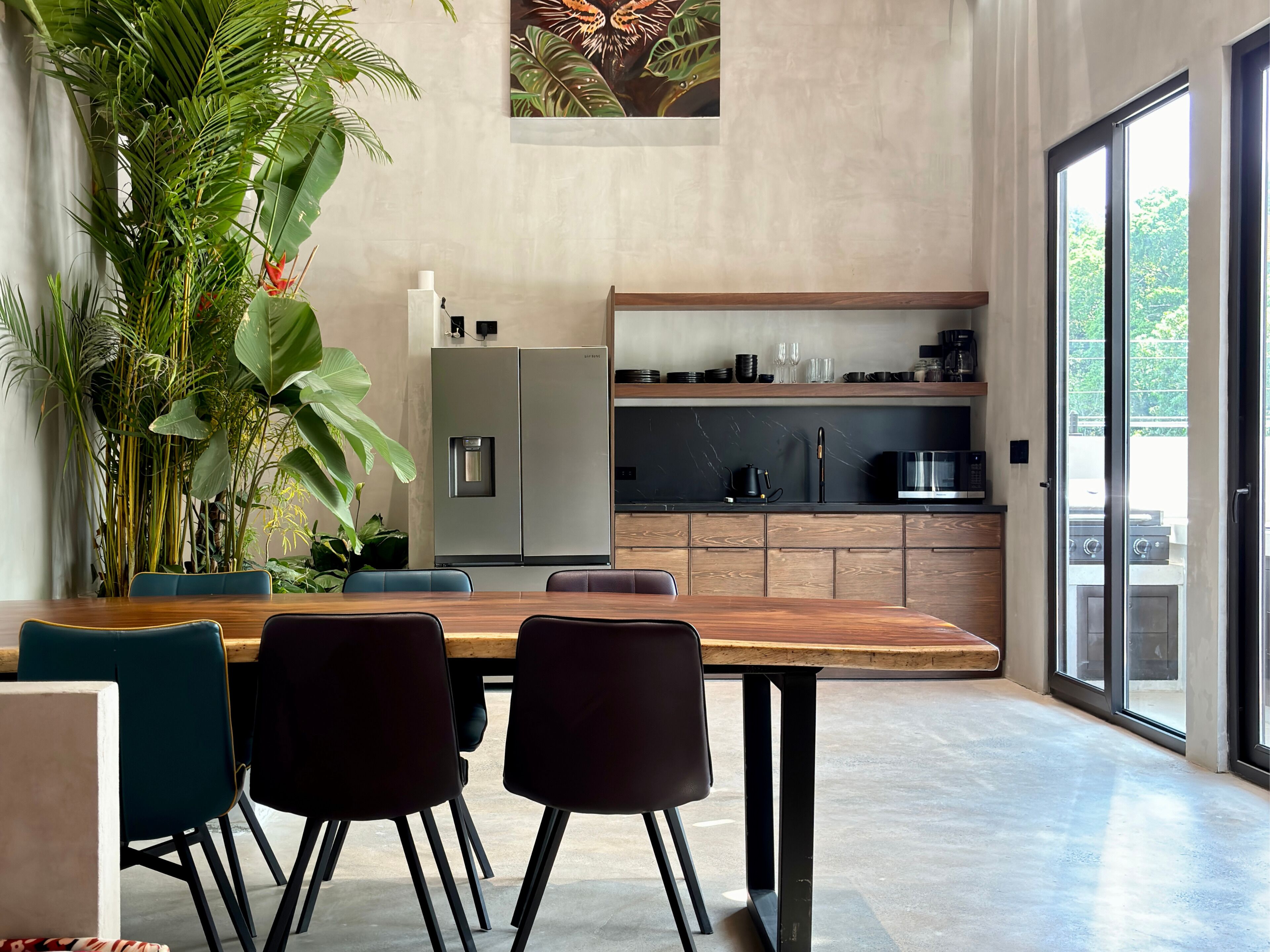 Una cucina moderna con frigorifero integrato, microonde e piano cottura. C'è una zona pranzo con tavolo e sedie in legno, e un'ampia pianta in vaso.