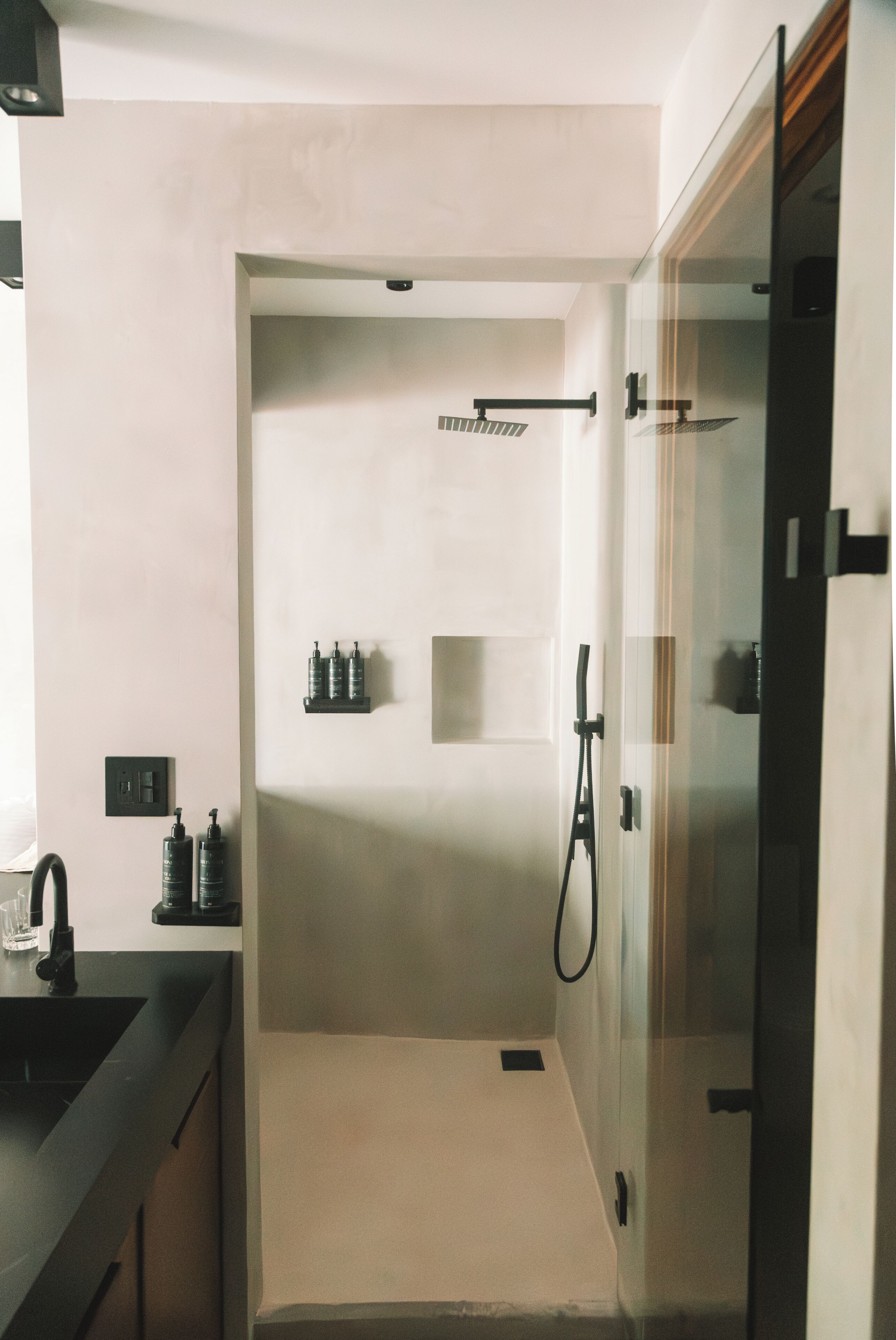 Un baño moderno con cabina de ducha de vidrio, un lavamanos con grifo y dos dispensadores de jabón en la pared.